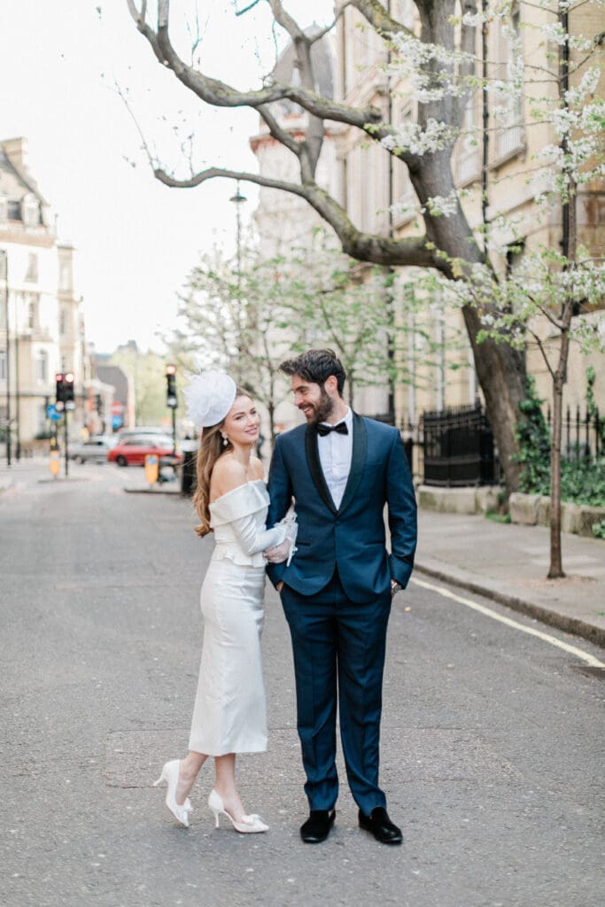 Bride tenderley holding the arm of her groom whilst smiling at the camera on the streets of London.