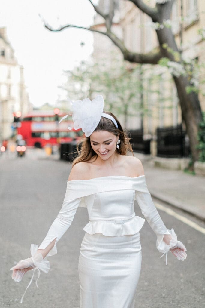 Bride playfully standing on the streets of Chelsea in her bridal dress with a red London bus blurred in the background behind her