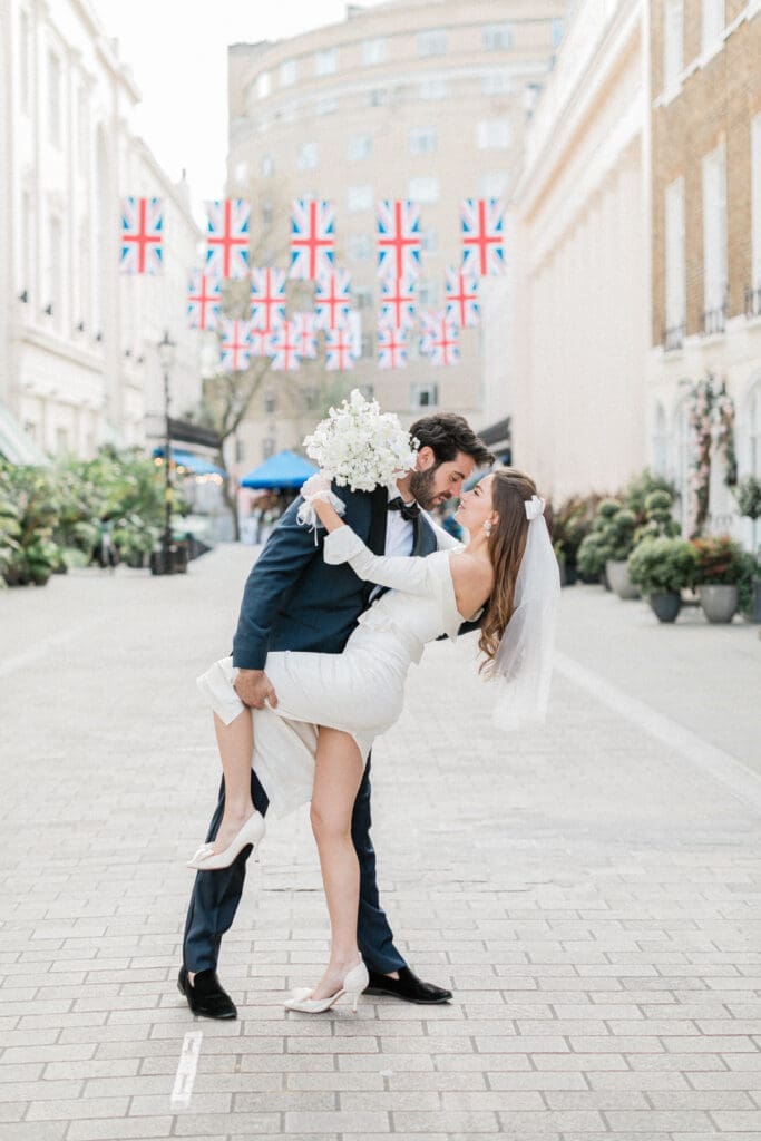 Bride and Groom is a romantic embrace on the streets of Chelsea with Union Jack flags handing above in the background.