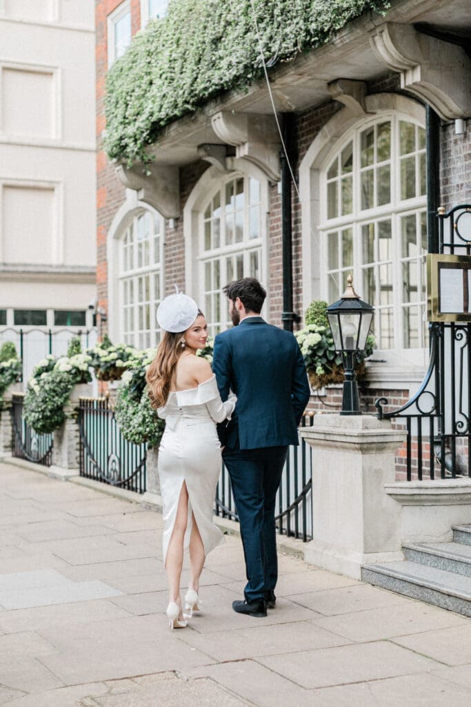 Bride and groom walking with arms entwined, outside the Goring hotel with the bride looking back towards the camera.