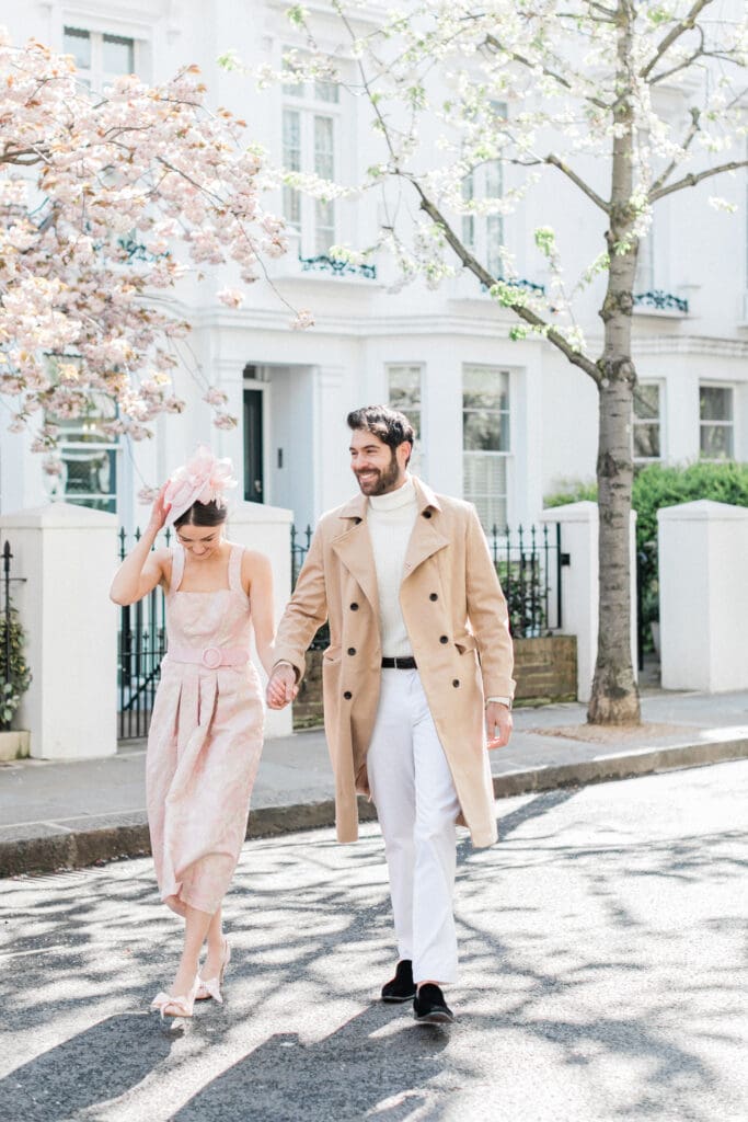 A couple walking the streets of Notting Hill with a pink blossom tree behind them for their engagement shoot in London
