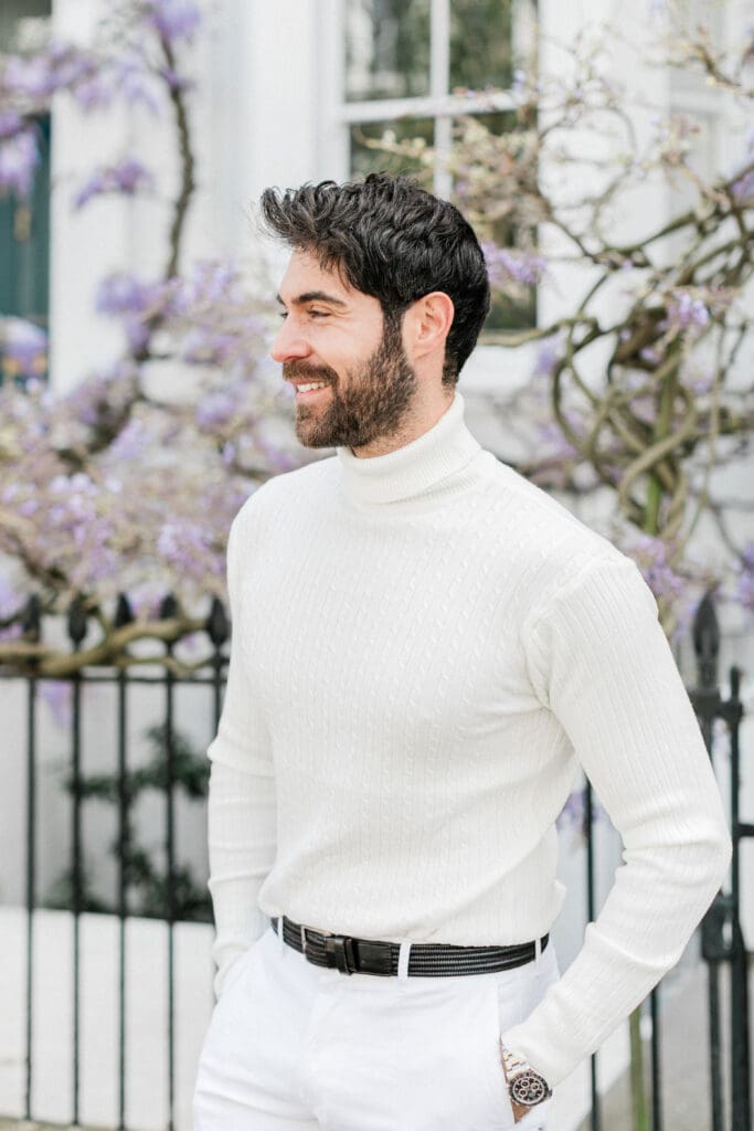 The groom posing for her engagement shoot with a backdrop of wisteria behind her for her engagement shoot in London.