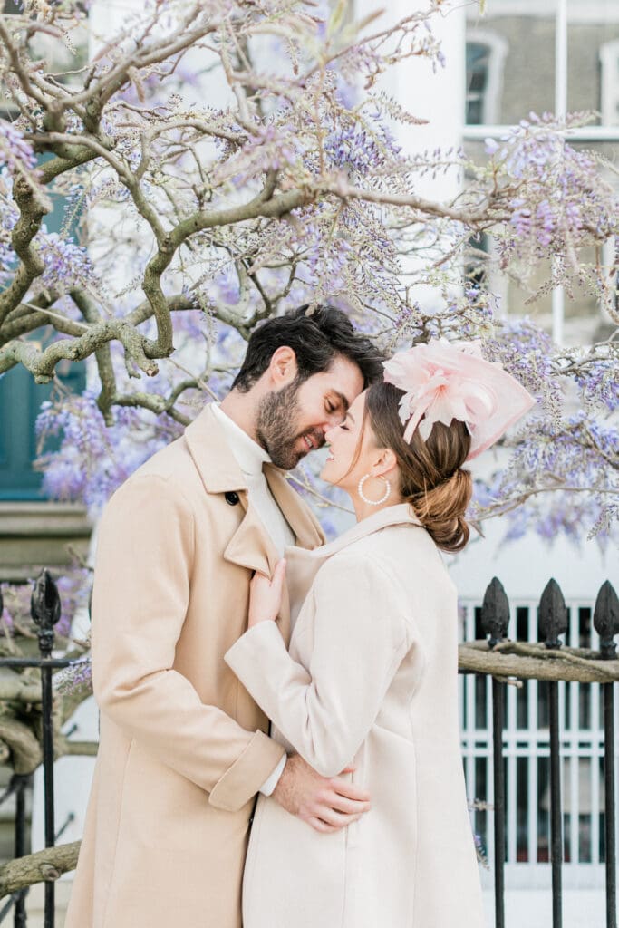 A couple leaning into a romantic kiss for their engagement shoot in London with purple wisteria behind them.