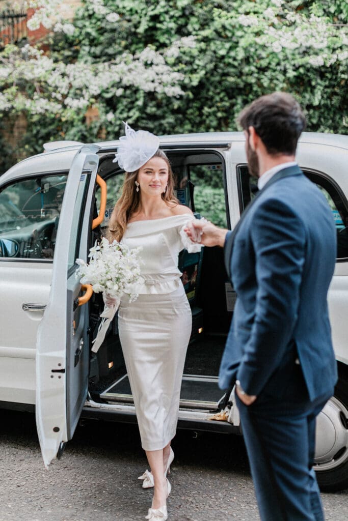 Groom taking the hand of his bride as she steps out of a London taxi.