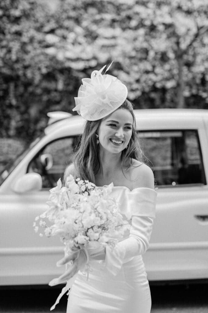 Bride smiling whilst holding her bridal bouquet with a London taxi behind her.
