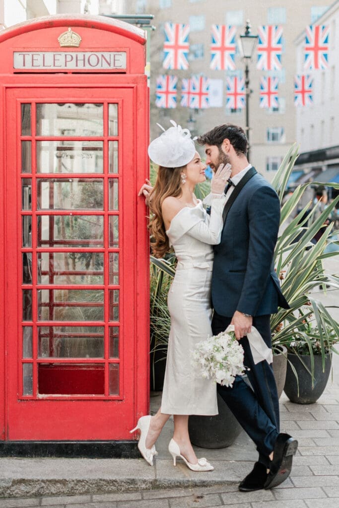 Bride and Groom in a romantic embrace looking at each other whilst leaned against a red London telephone box.