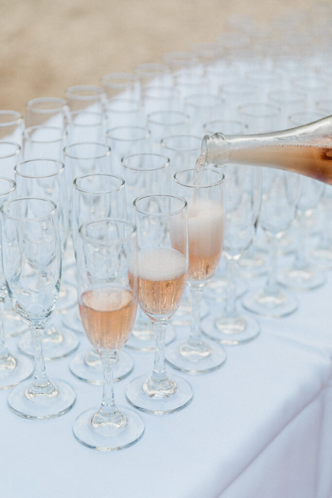 Champagne glasses being poured and ready to be served at outdoor wedding reception in Greece.