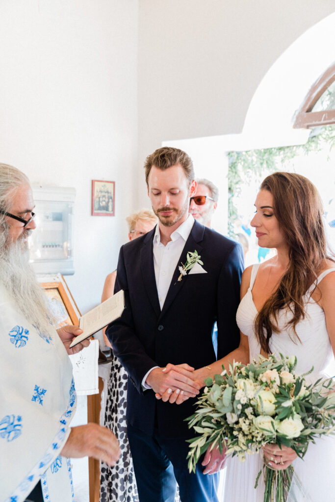 Bride and groom standing in front of the priest in Greek wedding ceremony.
