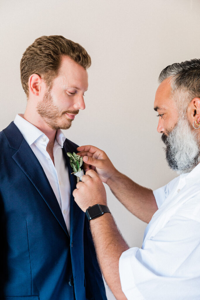 The groom having his buttonhole put on ahead of his Greek wedding in Ithaca.