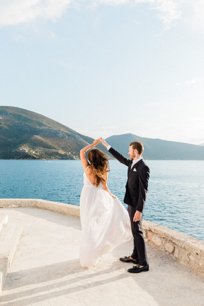 The groom spinning his bride around alongside the sea with a mountain view background at their wedding in Ithaca.