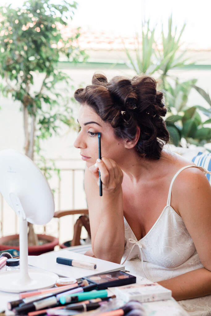 A close up of the bride getting ready ahead of her wedding day in Ithaca and applying her own makeup with her hair pinned in curls.