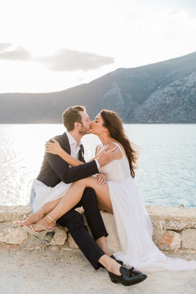 The bride and groom kissing each other whilst sitting down with the bride's legs over the grooms legs. A mountain view is in the background behind them.